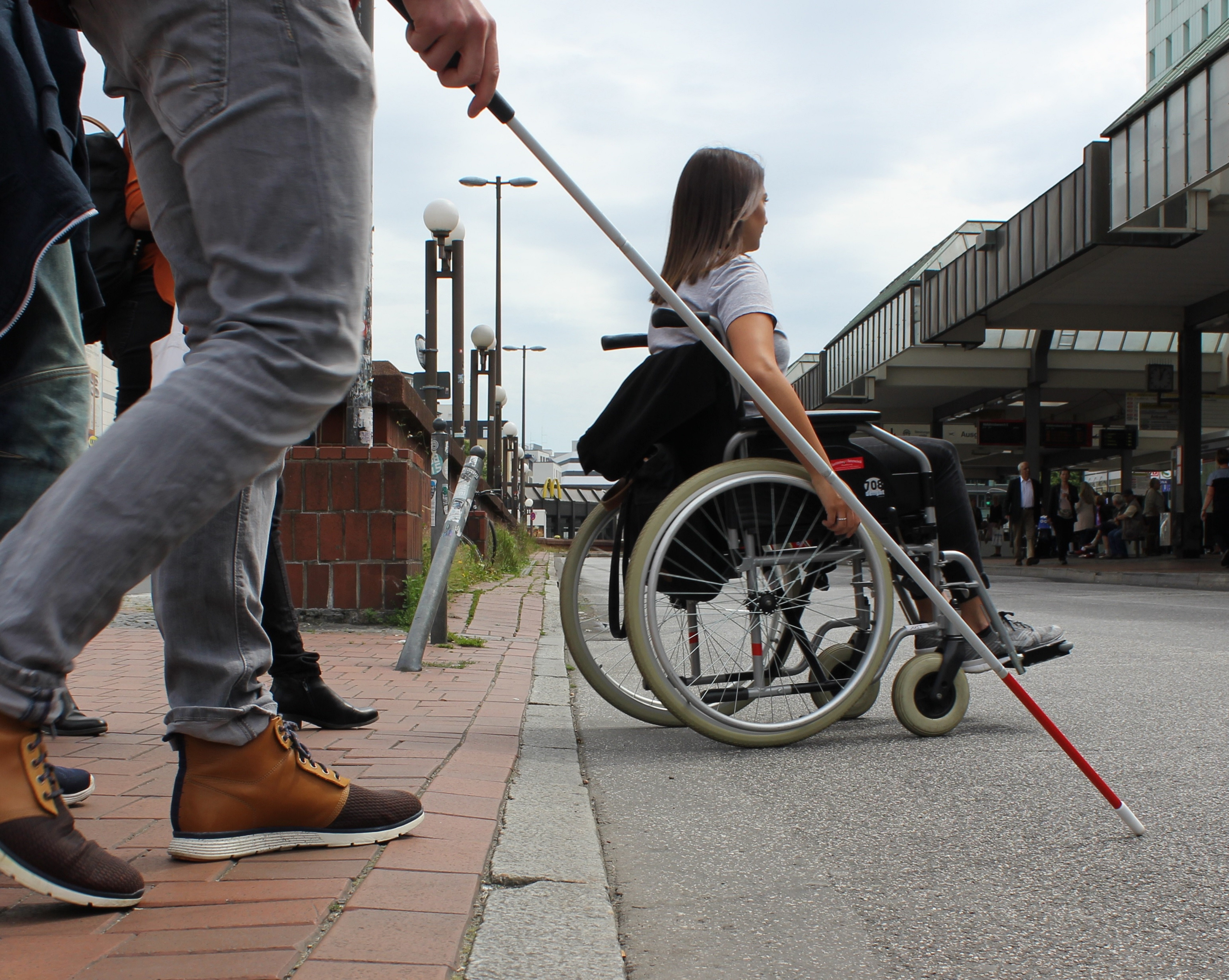 Frau mit Rollstuhl und Person mit Langstock überqueren Straße