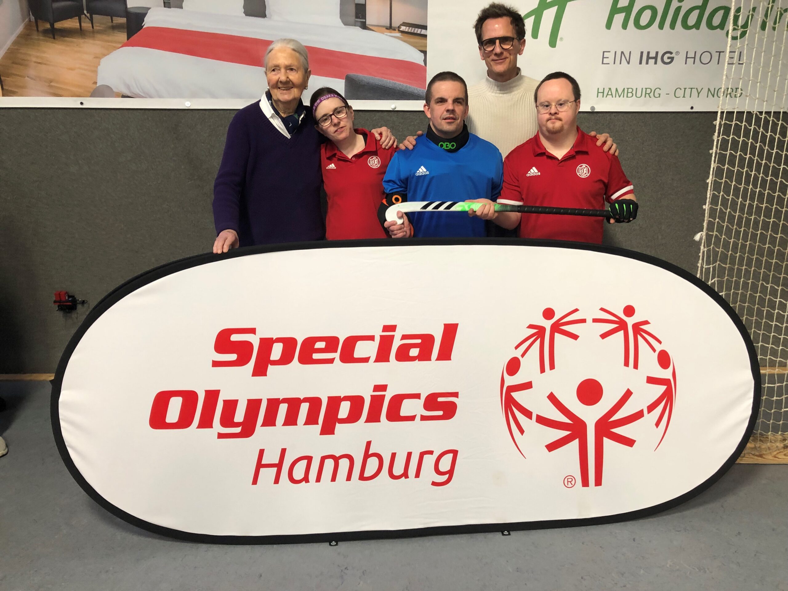 Greta Blunk und Hockeyspieler:inenn stehen hinter einem großen Banner von Special Olympics Hamburg.