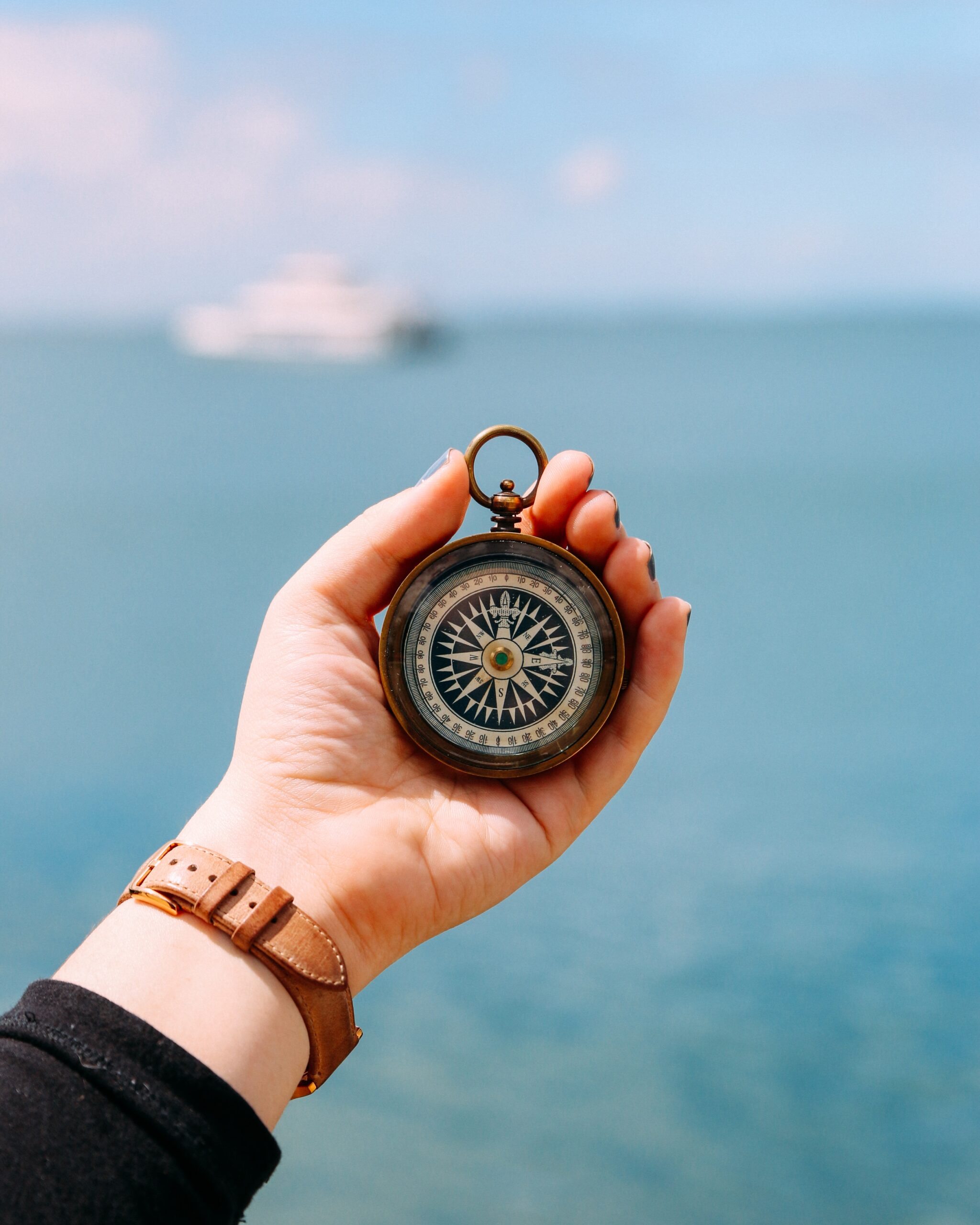 Frauenhand hält Kompass, im Hintergrund Meer und Schiff