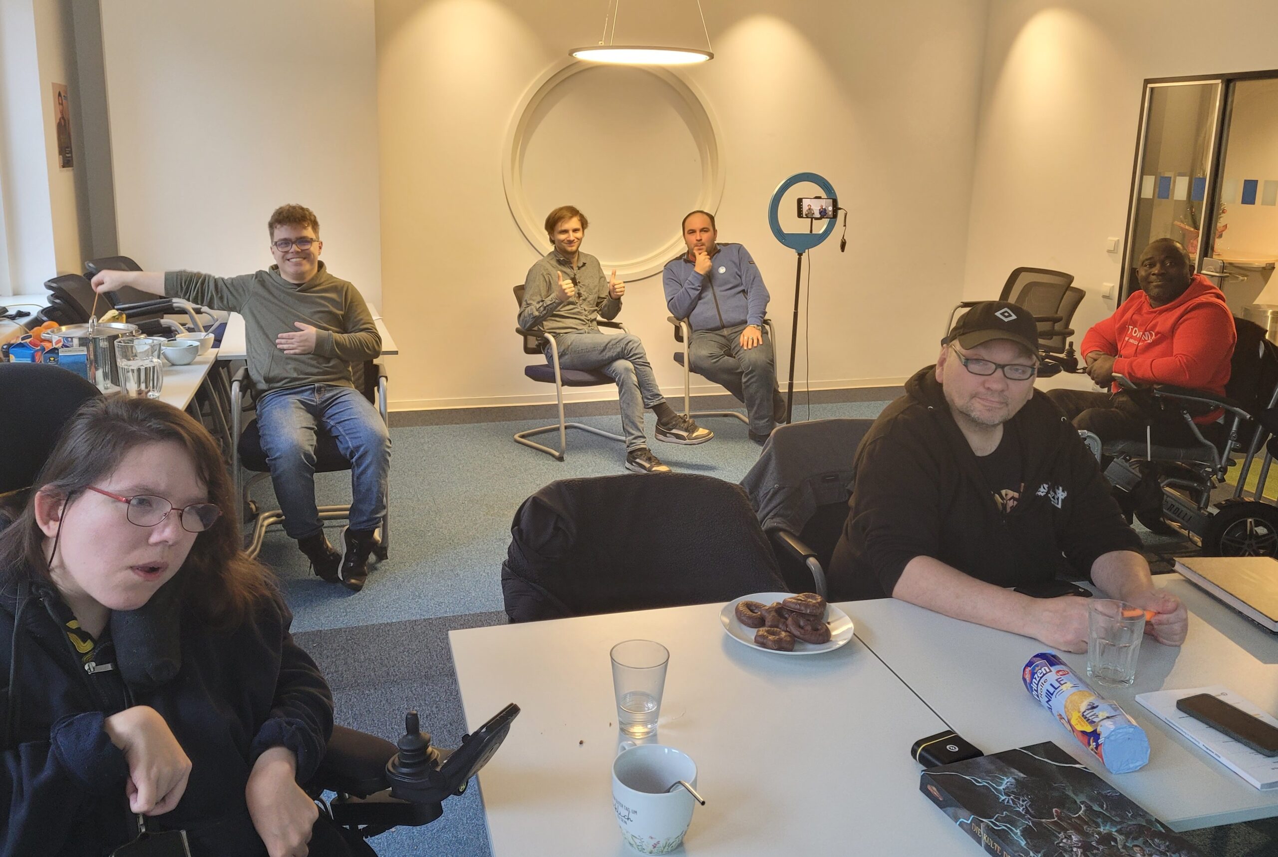 Sechs junge Menschen sitzen in einem Raum mit Ringlicht, gucken in die Kamera, machen Pause.