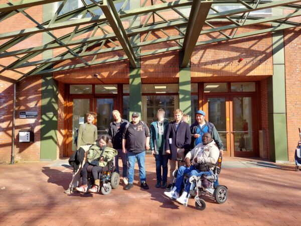 Eine Gruppe von Menschen vor einem überdachtren Gebäude aus rotem Backstein