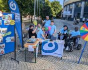 im Freien: Ein Tisch mit Materialien, eine Gruppe von Leuten dahinter, eine Foto-Wand, ein buntes Glücksrad